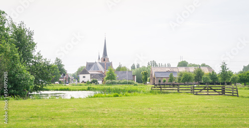 Classic view of a dutch village with church tower, water and green pastures