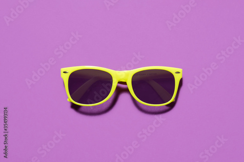 Yellow sunglasses flat lay / top view on a purple background with a centre composition