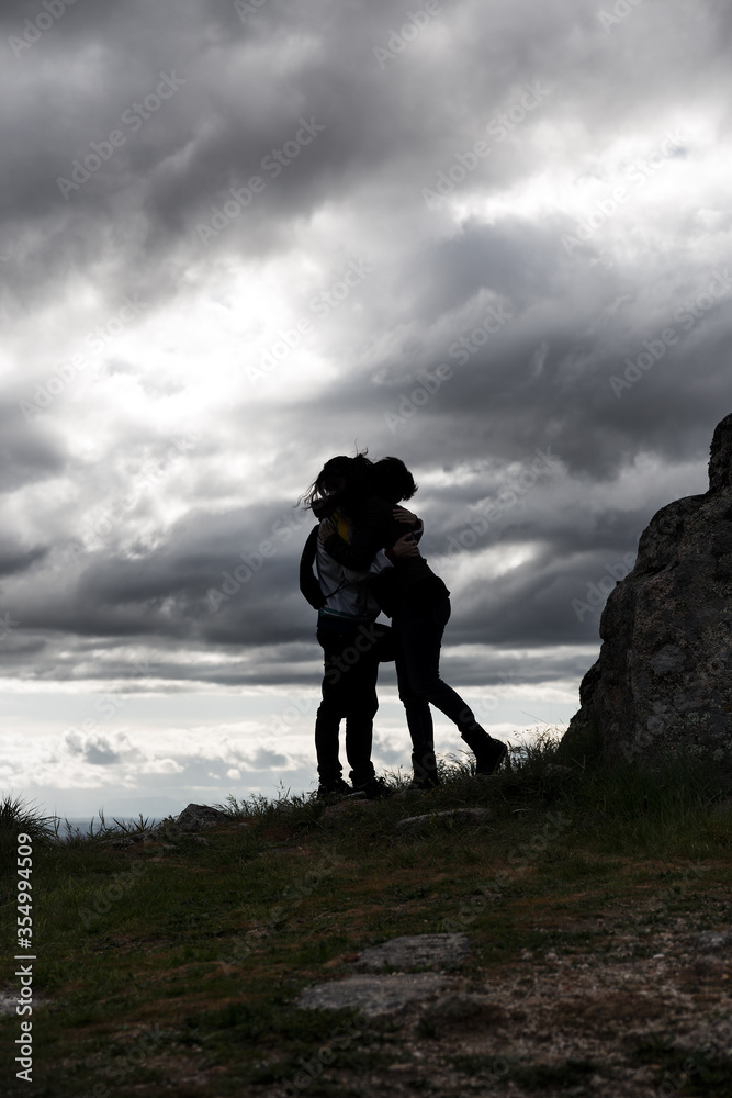 Silhouette hug of mother and son with cloudy sky background