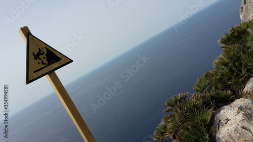 Attention, steep cliffs sign at the coast of Mallorca with a view of rocks and the Mediterranean Sea, Spain
