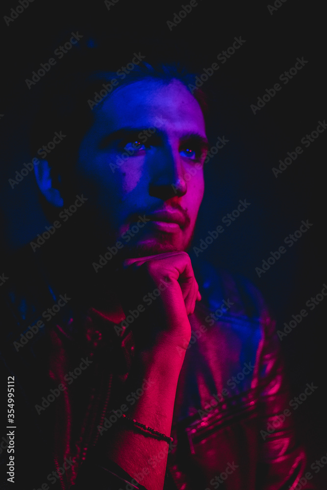 Man in his 30s posing to the camera with blue and red lighting, close up portrait 
