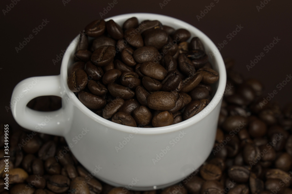White mug with coffee grains sprinkled with coffee grains on a background White mug with coffee grains sprinkled with coffee grains on a background