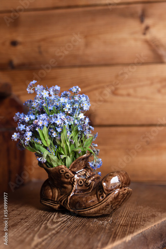 Ceramic shoe with a bouquet of forget-me-nots. On a wooden background.