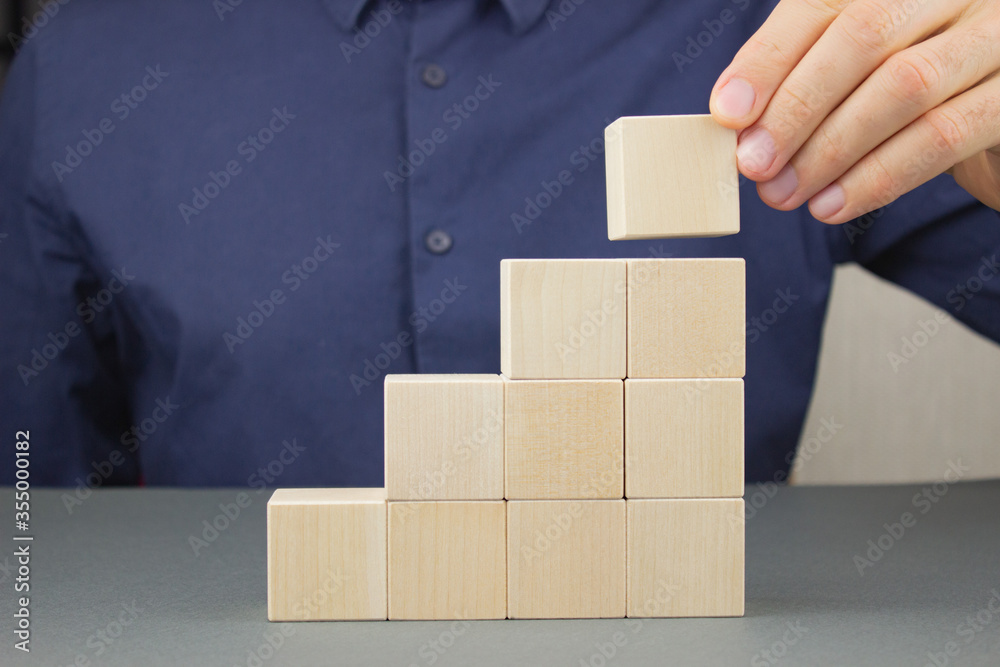 Closeup of businessman making a pyramid of wooden cubes at an office desk. The concept of financial planning and growth. Closeup of businessman making a pyramid of wooden cubes at an office desk. The concept of financial planning and growth.