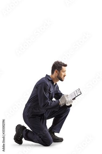 Fotografie, Obraz Auto mechanic worker in a uniform kneeling and writing a document
