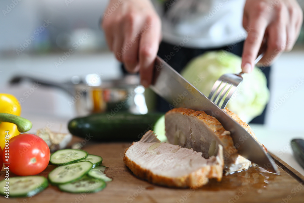 Hands chop ready baked pork meat and vegetables