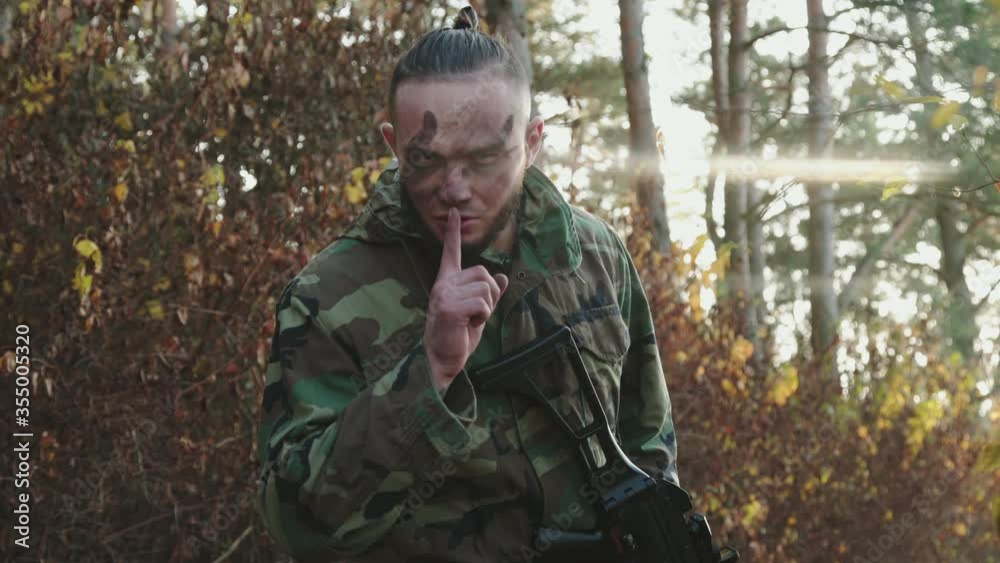 A soldier returns to camera with a rifle, puts finger to lips to show silence A soldier returns to camera with a rifle, puts finger to lips to show silence