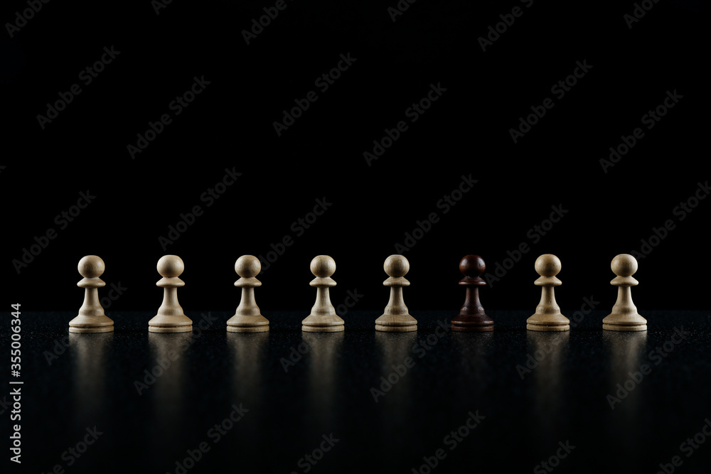 chess concept of out of the ordinary. black pawn in in the row of white pawns on black background
