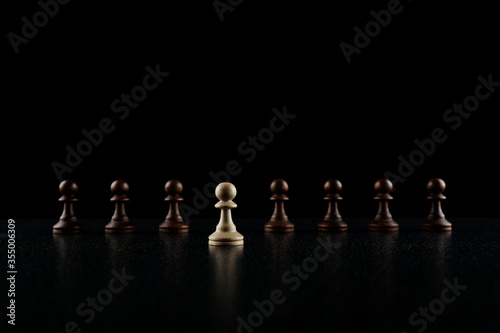 chess concept of out of the ordinary. black pawn is in the row of white pawns on black background.