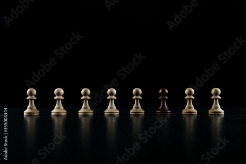 chess concept of out of the ordinary. black pawn in in the row of white pawns on black background