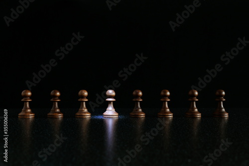 black pawns in a row on a black background. selective highlighting on one of the figures from a row. individuality concept
