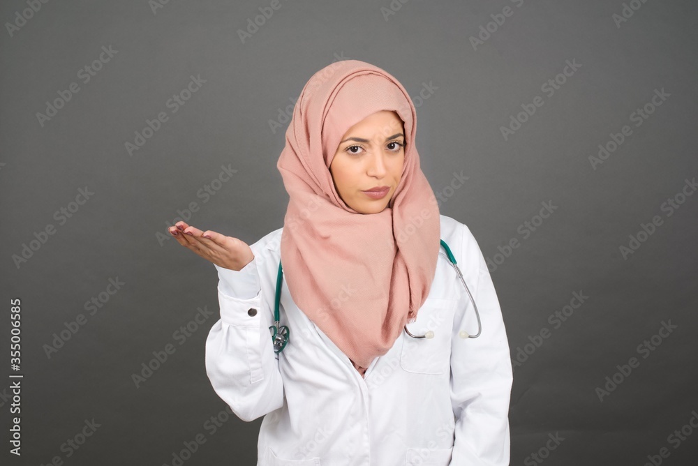 What the hell are you talking about, nonsense. Studio shot of frustrated muslim doctor female gesturing with raised palm, frowning, being displeased and confused with dumb question over gray wall. What the hell are you talking about, nonsense. Studio shot of frustrated muslim doctor female gesturing with raised palm, frowning, being displeased and confused with dumb question over gray wall.