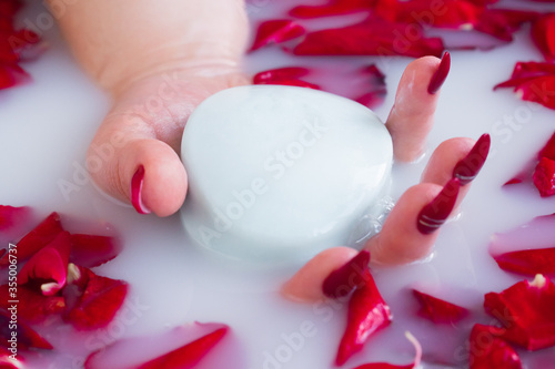 Female hand hold soap against the background of milk or white water with rose petals