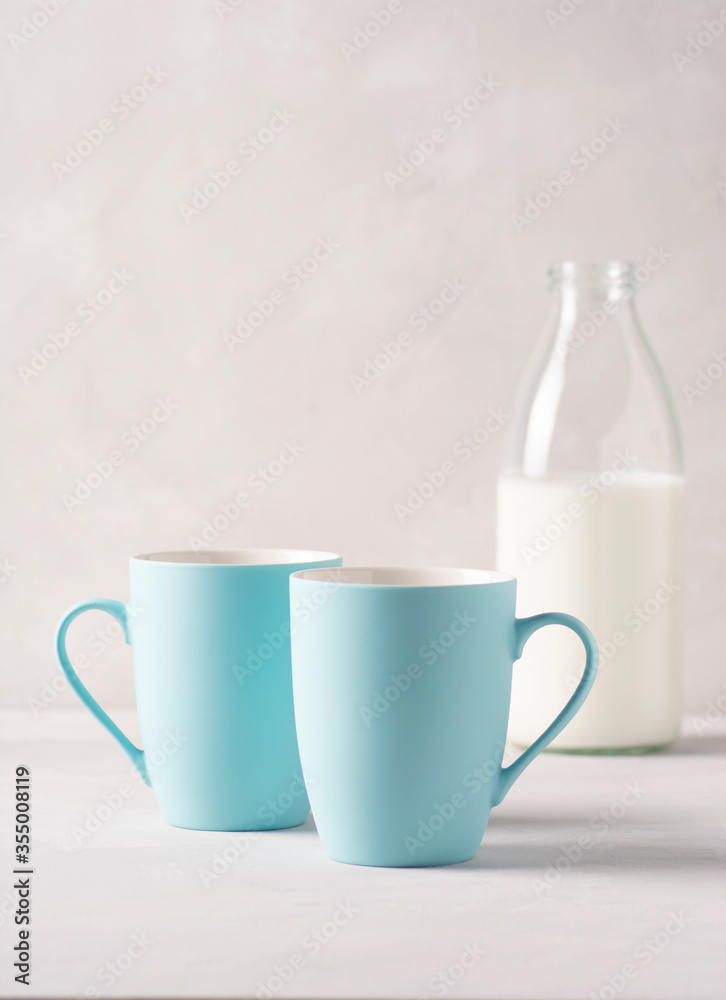 Two blue mugs and a bottle of milk are standing on a gray concrete table. Vertical orientation, there is a copy space. Two blue mugs and a bottle of milk are standing on a gray concrete table. Vertical orientation, there is a copy space.