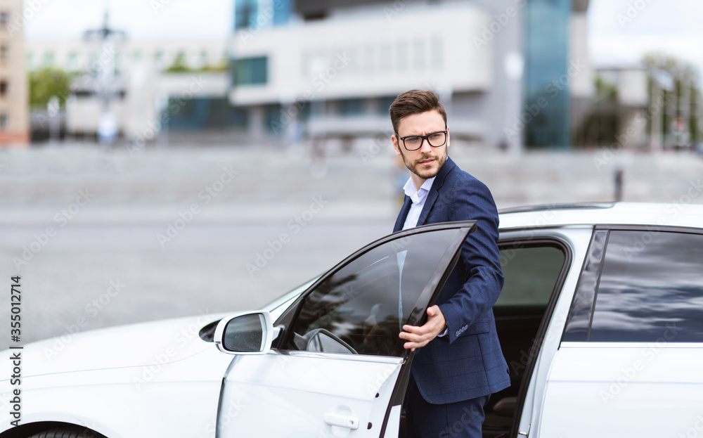 Attractive Caucasian entrepreneur in stylish suit getting in his car at downtown area, copy space
