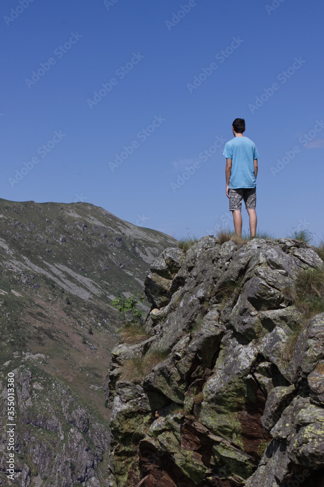 A boy standing on a spur of rock observes a panorama of morenic hills