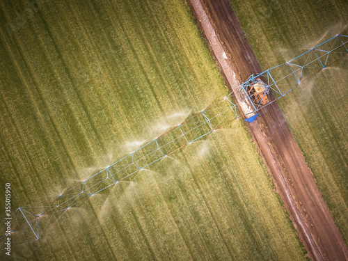 Aerial view of farming tractor spraying on field with sprayer, herbicides and pesticides at sunset. photo