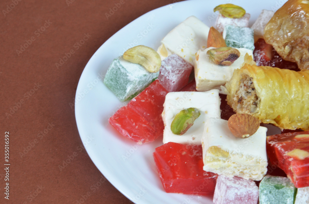 Tasty oriental sweets baklava, turkish delight on a plate on a dark black brown background Tasty oriental sweets baklava, turkish delight on a plate on a dark black brown background