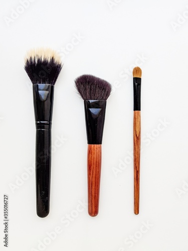 Cosmetic brushes with wooden brown handles and brown lint on a white background.