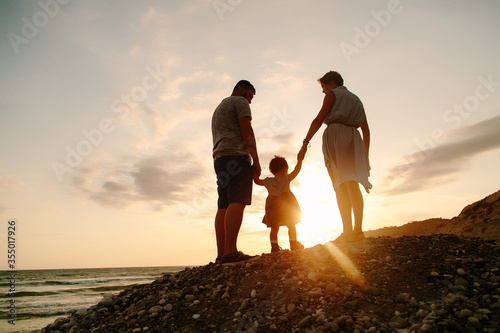 Happy family - father  mother  baby daughter hold hands. sunset  sea. Active parents and people outdoor activity on summer  vacations with children. High quality photo