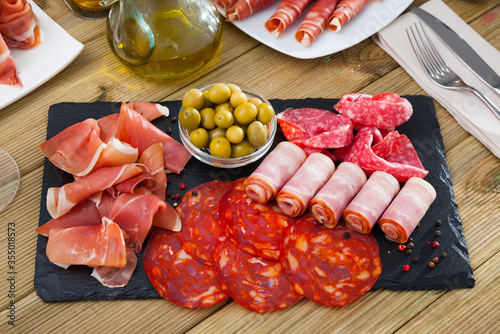 Slices of gammon, chorizo, salami, bacon on slate board