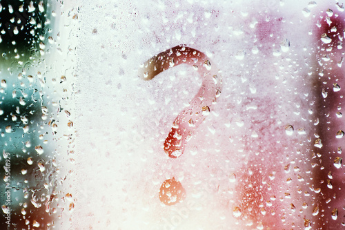 Drops of morning summer rain on a fogged window with a question mark drawn on a blurred background of nature in the daytime. Summer vacation and travel concept