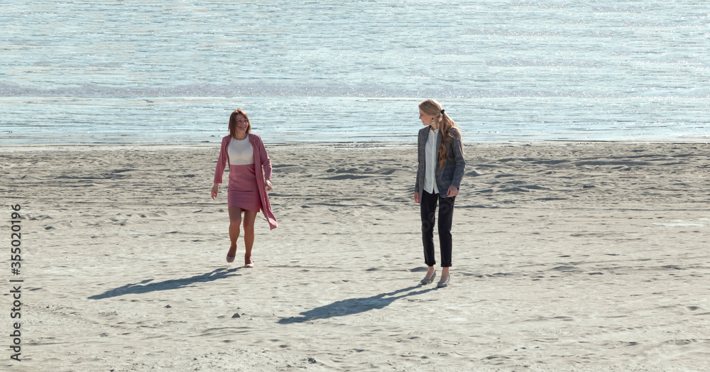two women in office clothes run along the sand of the sea shore. two women in office clothes run along the sand of the sea shore.