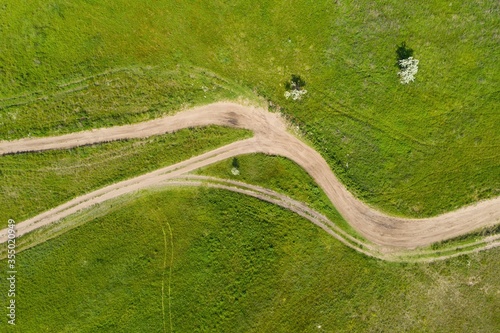 Rural road surrounded with green grass. Aerial view.
