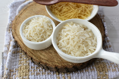 Short pasta spaghetti angel hair and uncooked rice displayed in containers on white background