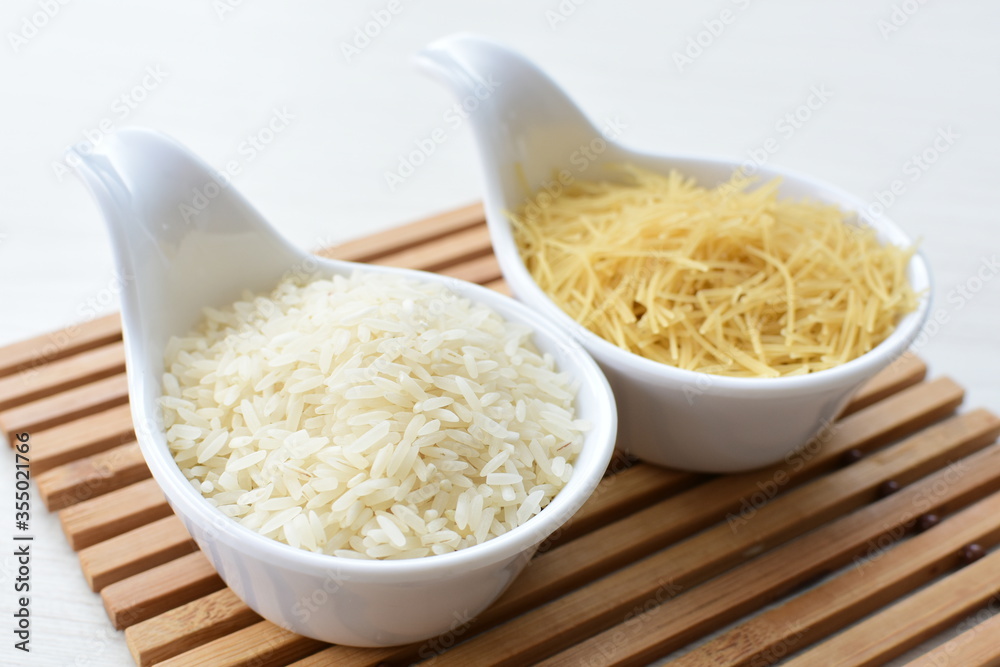 Short pasta spaghetti angel hair and uncooked rice displayed in containers on white background Short pasta spaghetti angel hair and uncooked rice displayed in containers on white background