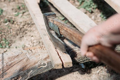 Old metal axe stuck in the wooden plank. Hard manual work