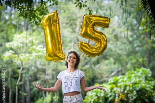 brazilian teenager girl in the park trowing up  balloons number 15  in celebration of her fifteenth birthday