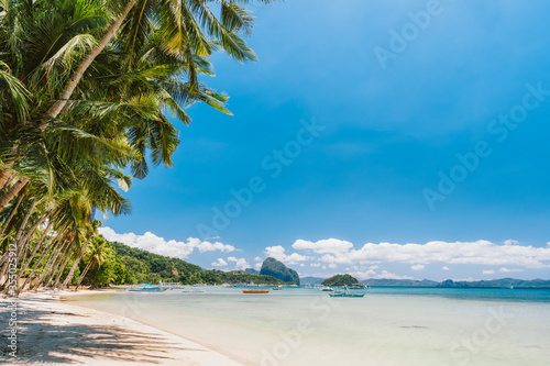 Palm trees of Corong Corong beach with traditional boats and blue sky in El Nido, Palawan island, Philippines