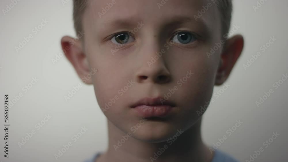 A closeup portrait of a young blonde caucasian man-child standing motionless in front of the white background looking in camera with no emotions on his face