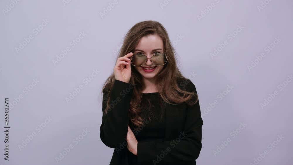 Young attractive brunette woman in a black t-shirt and sweater on white background, stylish female in sunglasses winks. Fashionable, modern people Young attractive brunette woman in a black t-shirt and sweater on white background, stylish female in sunglasses winks. Fashionable, modern people