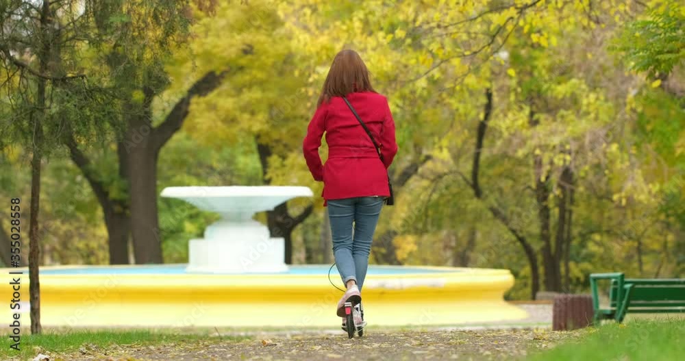 The girl rolls on the white kick scooter in the park near the dry fountain in the fall.