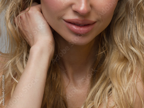 Close-up of woman's lips with fashion natural beige lipstick makeup. Macro sexy pale lipgloss make-up . Gentle pure skin and wavy blonde hair. Cosmetology, Spa, increase in lips