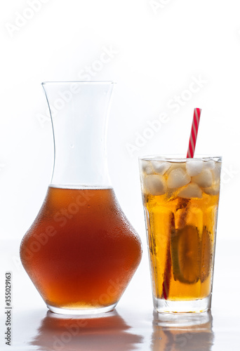 Iced tea with straw, ice cubes and sliced lemon and a glass bottle over white background