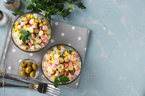 Salad with ham, olives, corn and pineapples in transparent salad bowls on a light blue background, top view, Space for text