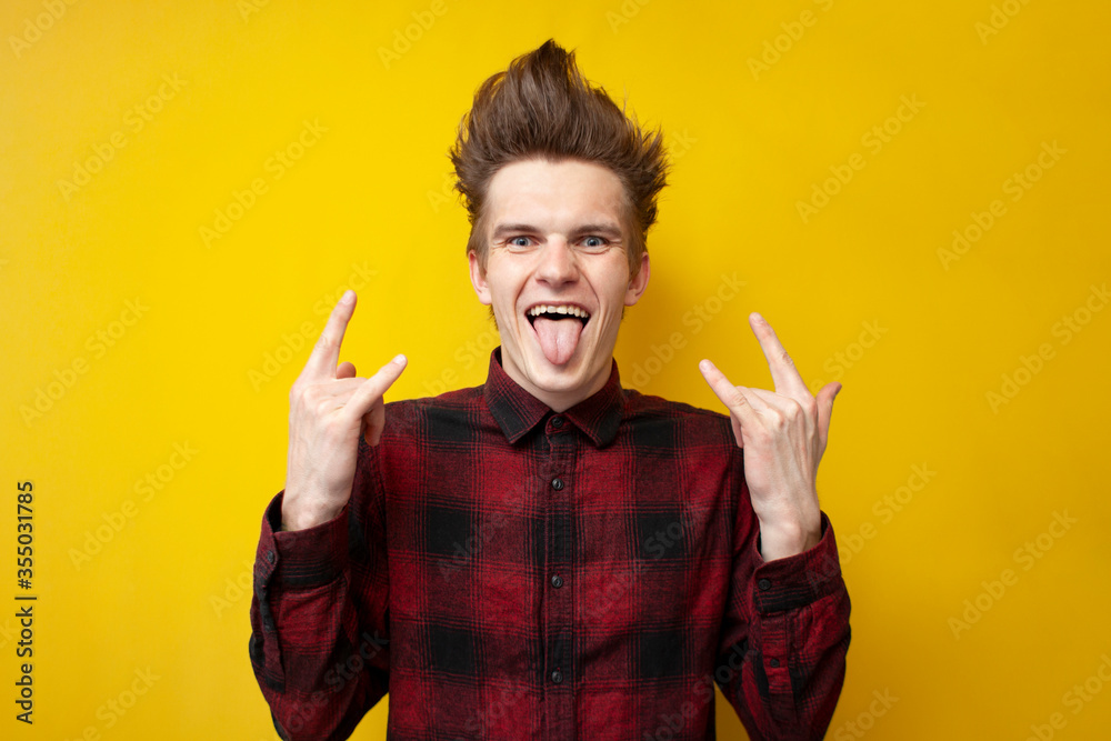 Φωτογραφία guy with a funny hairstyle shows a rock sign and screams on a yellow isolated ba