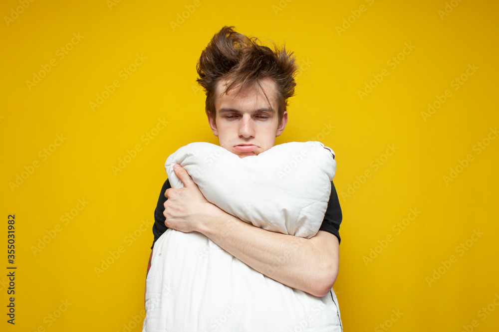 Fotografie tired sleepy student with a pillow is sad on a yellow background, the guy has a