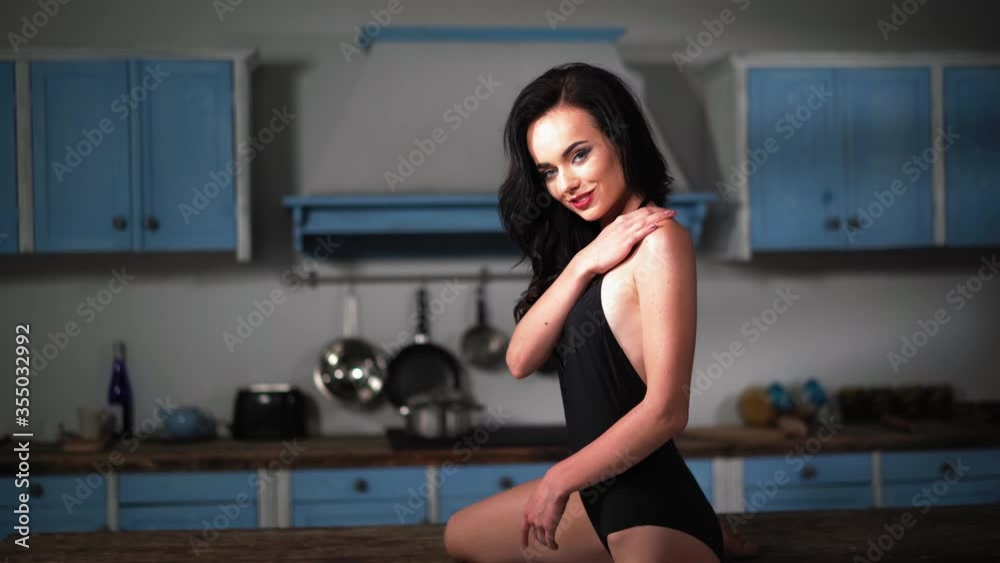Sexy lady in elegant black bodysuit sitting on kitchen island table with one leg on the floor gently touching arm. Lingerie concept. Prores 422. Sexy lady in elegant black bodysuit sitting on kitchen island table with one leg on the floor gently touching arm. Lingerie concept. Prores 422.