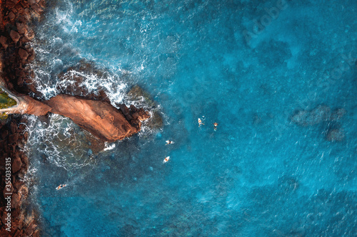 Aerial top view of cliff  surfers and turquoise transparent water 