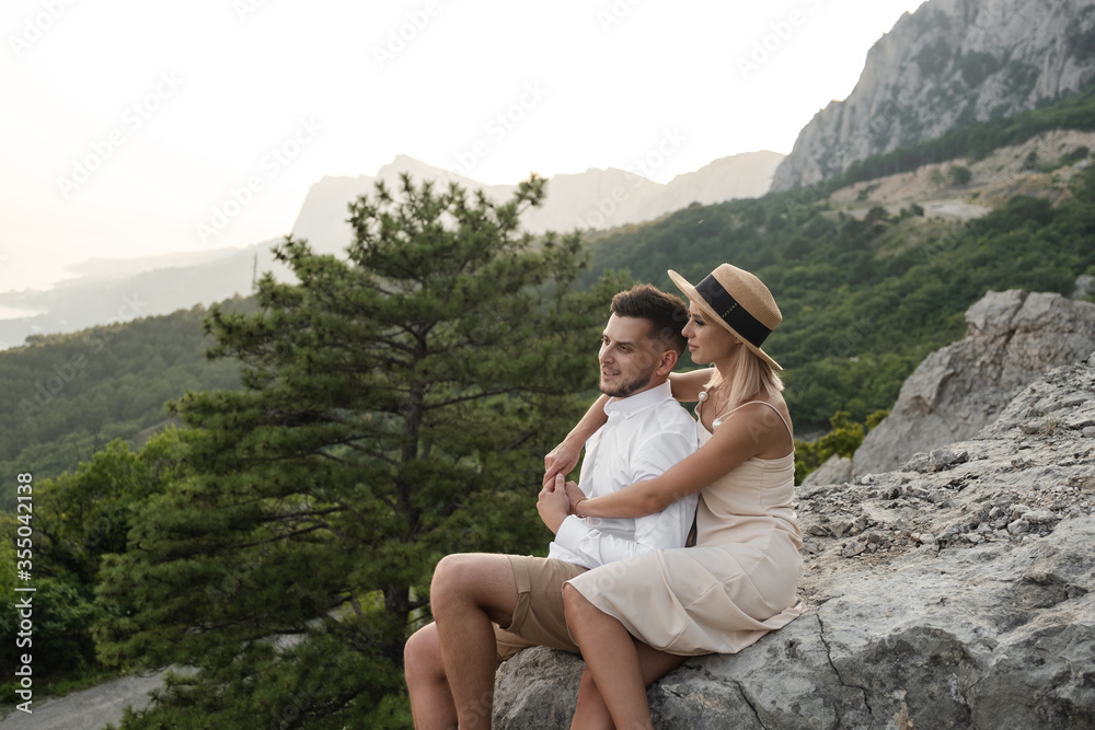 Young couple in love sitting on rock in the evening, beautiful dusk.