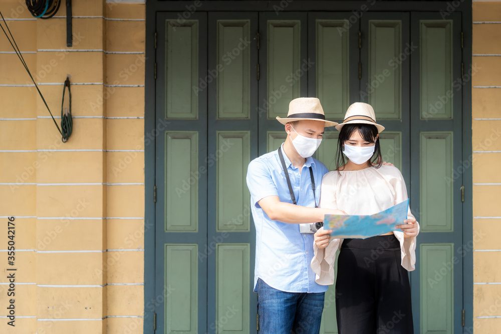 Asian couple happy tourists to travel wearing mask to protect from Covid-19 on they holidays and holding travel map in old town in Bangkok, Thailand