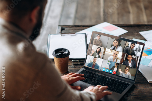 App for communication with employees. Online video conference. Young bearded man communicates via video call with business partners, he sits at the creative modern office space photo