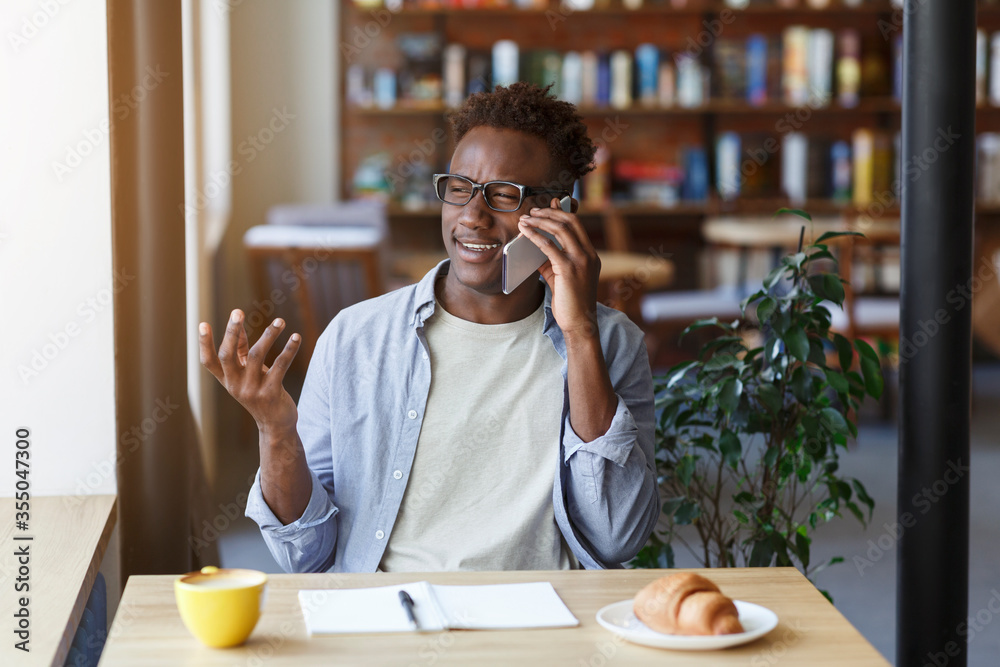 Funky African American guy making call on smartphone while studying in coffee shop Funky African American guy making call on smartphone while studying in coffee shop