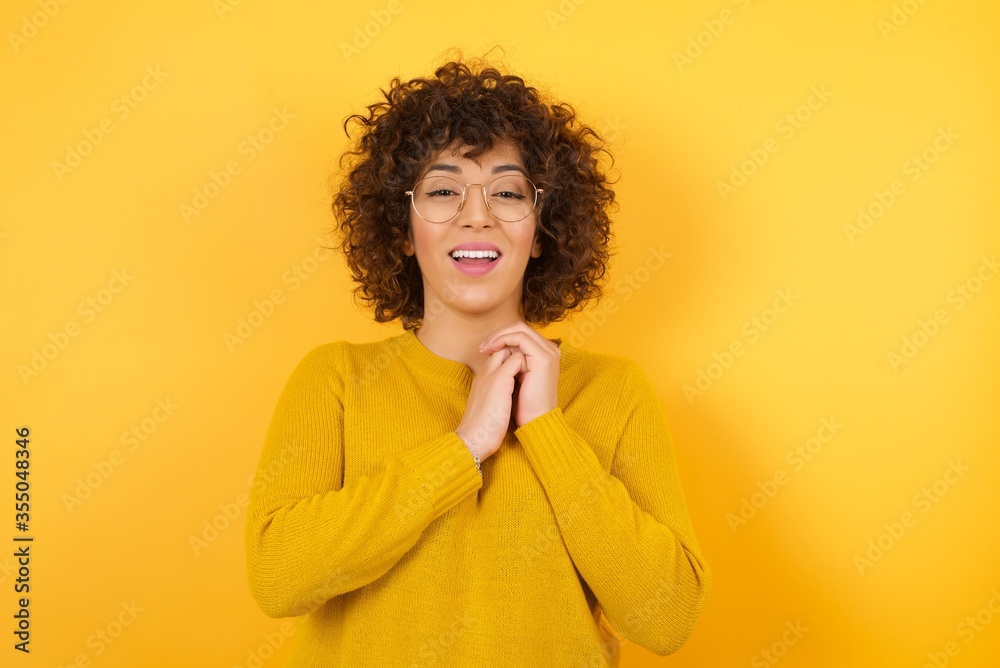 Positive adorable female model smiles happily, glad to receive pleasant news from interlocutor, keeps hands together, wears red shirt. People, retro style and emotions concept. Positive adorable female model smiles happily, glad to receive pleasant news from interlocutor, keeps hands together, wears red shirt. People, retro style and emotions concept.