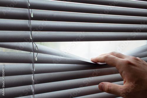 Man's hand revealing white venetian blinds with a finger.Hand opens jalousie. Isolation concept.