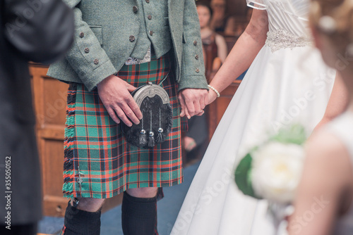 Scottish wedding couple hold hands at ceremony with man in kilt photo